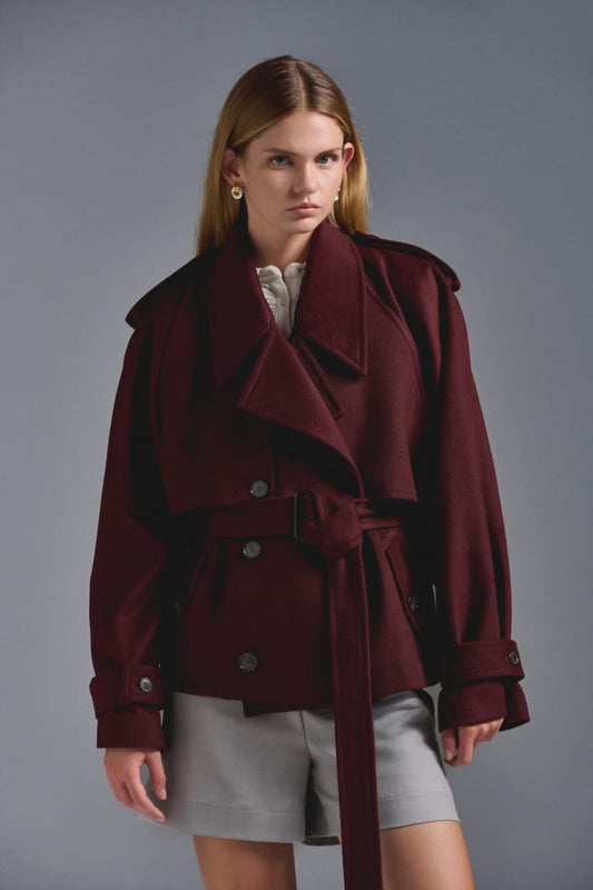 Chaquetón tipo trench corto. Oversize, confeccionado en paño sastre. Presillas en puño desmontables y ajustables. Charreteras en hombro y lazo del mismo paño desmontable. Botones al frente jaspeados y hebillas a tono. Composición: 50% Lana - 50% Poliéster. Interiormente forrado en tafeta jacquard.