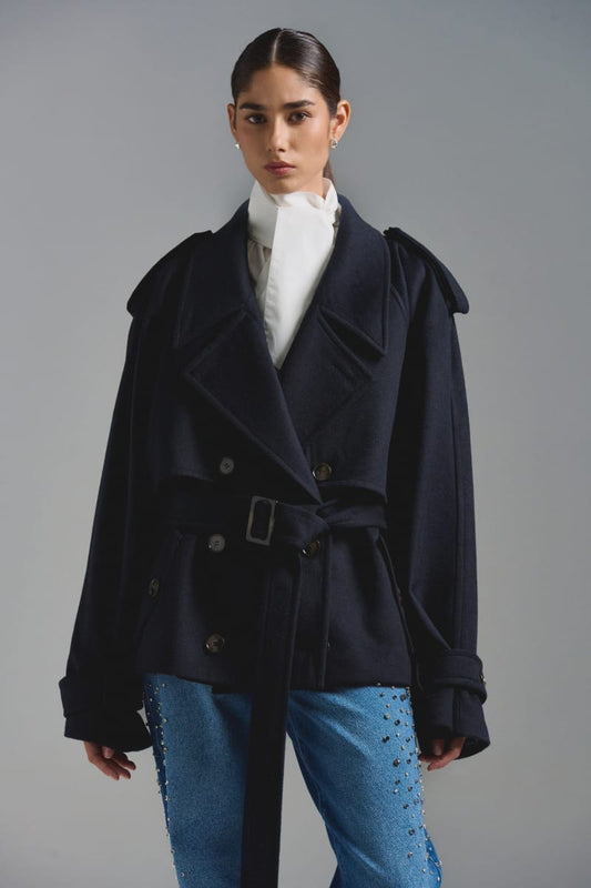 Chaquetón tipo trench corto. Oversize, confeccionado en paño sastre. Presillas en puño desmontables y ajustables. Charreteras en hombro y lazo del mismo paño desmontable. Botones al frente jaspeados y hebillas a tono. Composición: 50% Lana - 50% Poliéster. Interiormente forrado en tafeta jacquard.