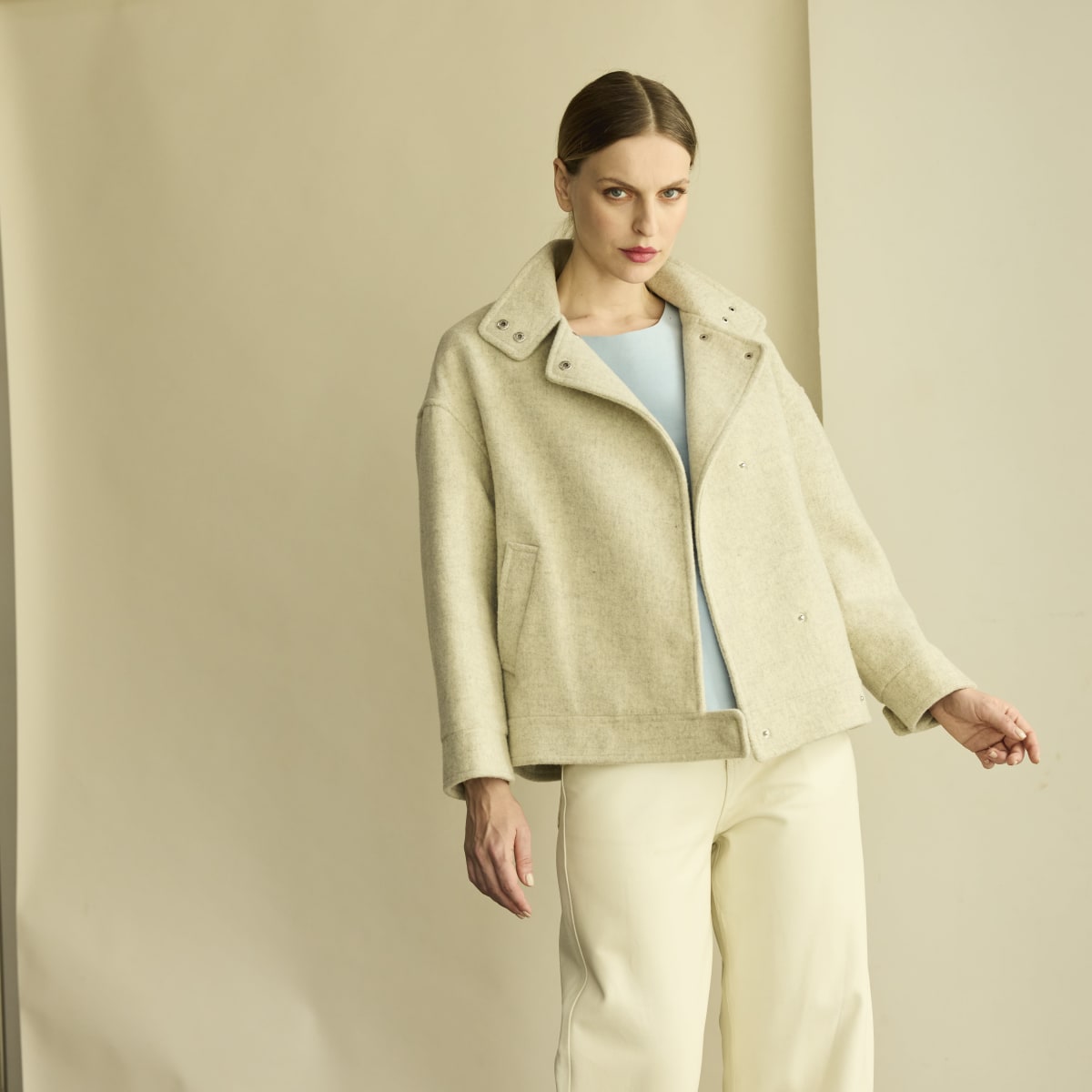 Chaqueta corta de paño gris claro. De silueta tipo bomber, confeccionado en paño sastre premium. Broches de presión en el frente y puños. Bolsillos laterales.