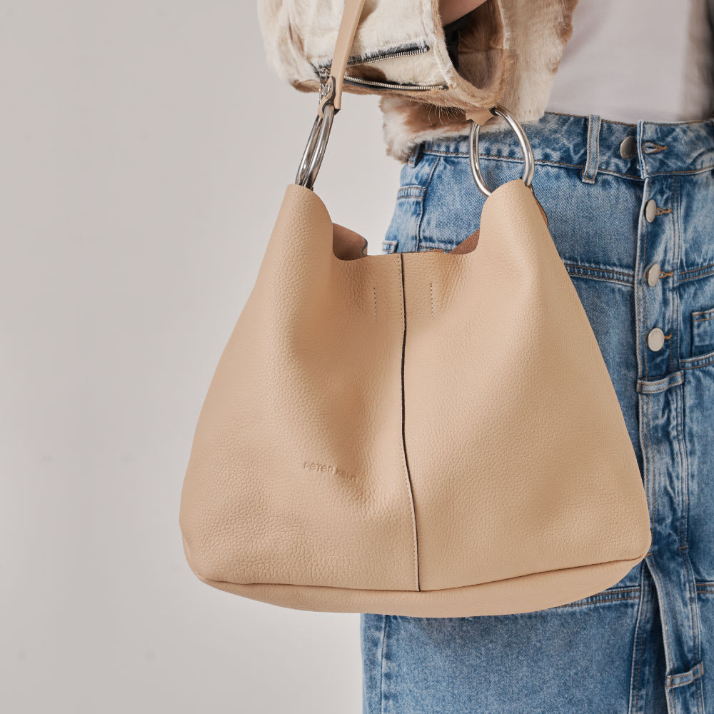 Bolso con herrajes ovalados, cuero graneado y correa que se adapta perfectamente al hombro. Billetera colgante (interior) y portallaves.