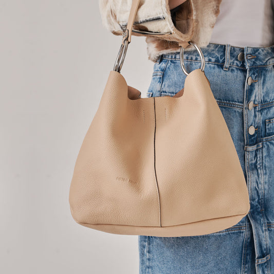 Bolso con herrajes ovalados, cuero graneado y correa que se adapta perfectamente al hombro. Billetera colgante (interior) y portallaves.